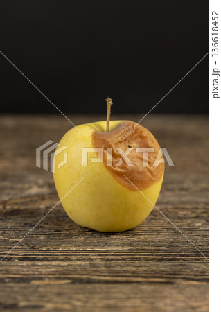 a whole yellow apple with a large orange spot during rotting, one rotting apple on a black wooden table made of pine wood 136618452