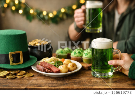 Friends toasting with green ale for Saint Patricks Day. Festive table with corned beef, cupcakes and lucky charms. 136619778