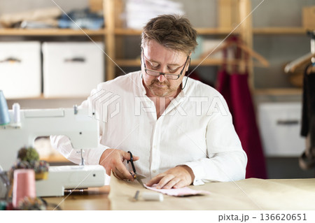 Middle-aged male dressmaker cutting cloth detail in sewing workshop Middle-aged male dressmaker cutting cloth detail in sewing workshop 136620651