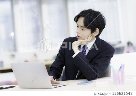 オフィスでノートパソコンで仕事をする困った顔のスーツを着た若い日本人男性 オフィスでノートパソコンで仕事をする困った顔のスーツを着た若い日本人男性 136621548