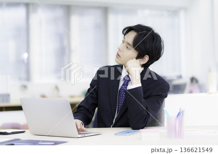 オフィスでノートパソコンで仕事をする困った顔のスーツを着た若い日本人男性 オフィスでノートパソコンで仕事をする困った顔のスーツを着た若い日本人男性 136621549