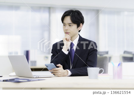 オフィスでノスマホを手に困った顔のスーツを着た若い日本人男性 136621554