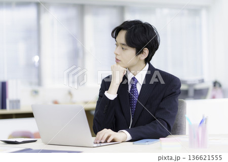 オフィスでノートパソコンで仕事をする困った顔のスーツを着た若い日本人男性 オフィスでノートパソコンで仕事をする困った顔のスーツを着た若い日本人男性 136621555