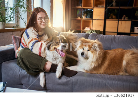 Woman sitting with two dogs on sofa in warm modern apartment. 136621917