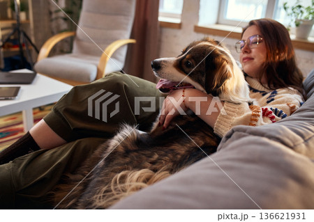 Woman resting on couch with dog in warm evening light. Woman resting on couch with dog in warm evening light. 136621931