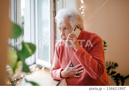 Old woman standing by window, making phone call. Old woman standing by window, making phone call. 136621997