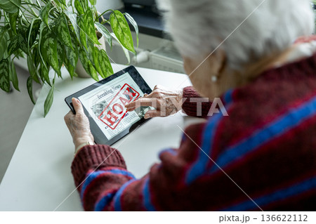 Old person recognizing fake news on digital tablet. 136622112
