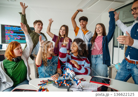 Group of high school students celebrating successful experiment with robotic hand. 136622125