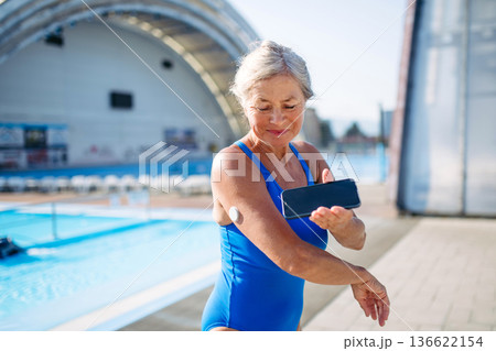 Diabetic senior woman checking glucose on her phone before swimming. 136622154