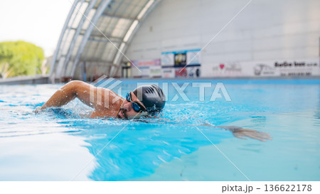 Focused swimmer performing crawl stroke in water. Focused swimmer performing crawl stroke in water. 136622178