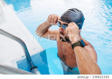 Male swimmer is preparing for swim in pool. Male swimmer is preparing for swim in pool. 136622183