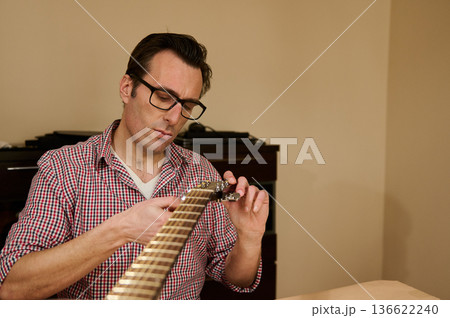 Man adjusting and changing guitar strings at a table, demonstrating guitar maintenance, repair and tuning techniques for musicians and instrument care. Man adjusting and changing guitar strings at a table, demonstrating guitar maintenance, repair and tuning techniques for musicians and instrument care. 136622240