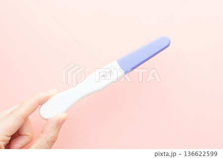 Pregnant woman holding a positive urine pregnancy test on pink background. Pregnancy test kit measure hCG levels in urine. 136622599