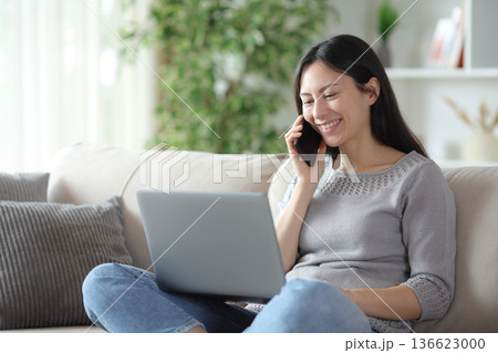 Happy asian woman talking on phone checking laptop content 136623000