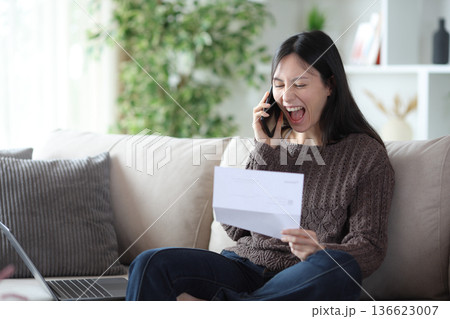 Excited asian woman checking letter calling on phone Excited asian woman checking letter calling on phone 136623007