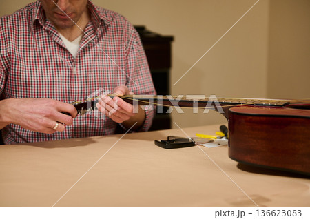 Man Changing Guitar Strings at Table - Guitar Maintenance and Repair Hands-On Man Changing Guitar Strings at Table - Guitar Maintenance and Repair Hands-On 136623083