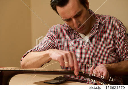 Man Adjusting Guitar Strings During Maintenance and Repair 136623270