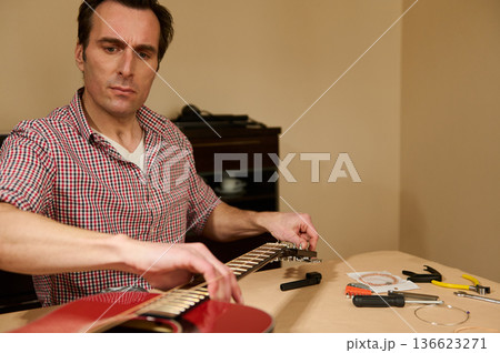 Man Changing Guitar Strings in Home Workshop - Guitar Maintenance and Repair Man Changing Guitar Strings in Home Workshop - Guitar Maintenance and Repair 136623271