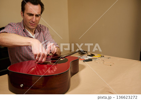 Man Repairing Acoustic Guitar Strings at Home - Guitar Maintenance and String Change 136623272