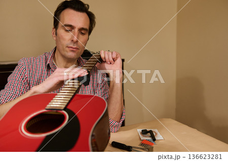 Man Adjusting Guitar Strings During Maintenance and Repair of Red Acoustic Guitar Man Adjusting Guitar Strings During Maintenance and Repair of Red Acoustic Guitar 136623281