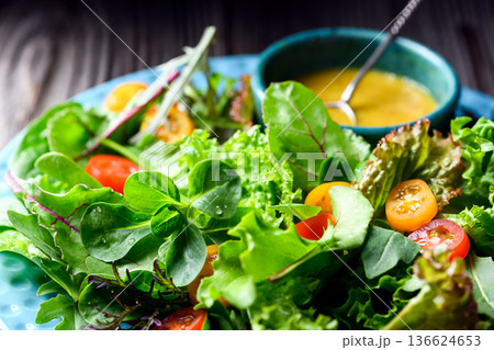 Mixed salad greens with cherry tomatoes and dressing on wooden table Mixed salad greens with cherry tomatoes and dressing on wooden table 136624653