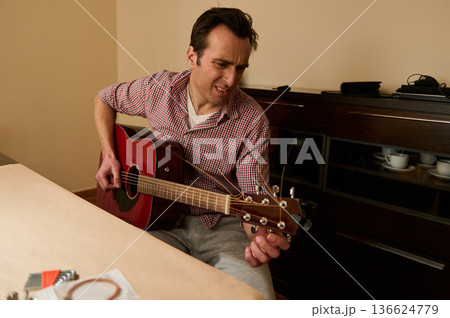 Man Changing Guitar Strings and Tuning an Acoustic Guitar for Maintenance and Repair Man Changing Guitar Strings and Tuning an Acoustic Guitar for Maintenance and Repair 136624779