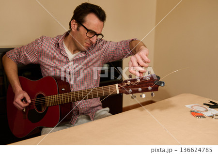 Man Changing Guitar Strings and Tuning an Acoustic Guitar at Home 136624785