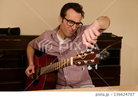 Man Adjusting Acoustic Guitar Strings - Guitar Maintenance and Repair Man Adjusting Acoustic Guitar Strings - Guitar Maintenance and Repair 136624787
