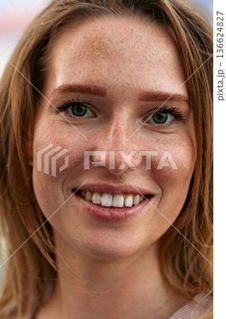 Young woman smiles and shows her teeth with freckles on her face in a close-up portrait 136624827
