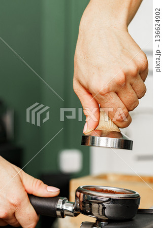 Barista prepares coffee by tamping ground coffee in portafilter at a cafe 136624902