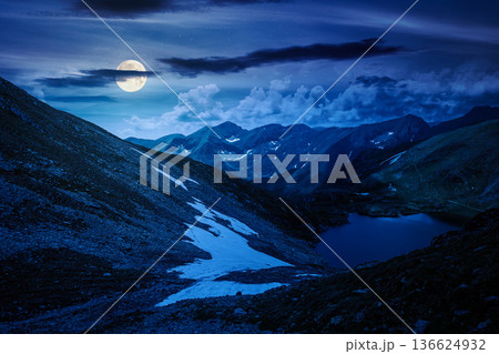 mountain lake in alpine summer landscape at night. beautiful view surrounded with clouds on a dark sky in full moon light. fresh water, snow and rocky slopes. mysterious remote fantasy highlands mountain lake in alpine summer landscape at night. beautiful view surrounded with clouds on a dark sky in full moon light. fresh water, snow and rocky slopes. mysterious remote fantasy highlands 136624932