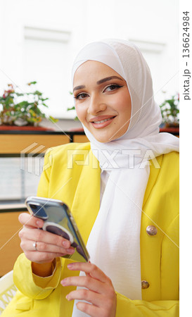 Woman in a yellow jacket using her smartphone in a bright indoor setting with plants Woman in a yellow jacket using her smartphone in a bright indoor setting with plants 136624984