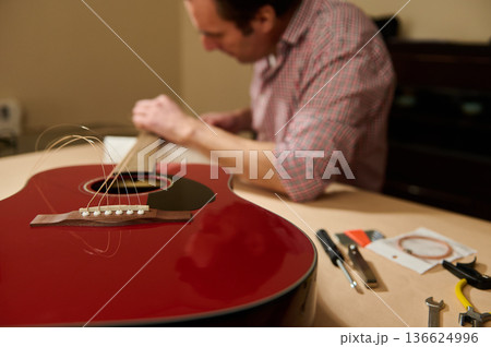 Man Changing Guitar Strings on Red Acoustic Guitar for Maintenance and Repair 136624996