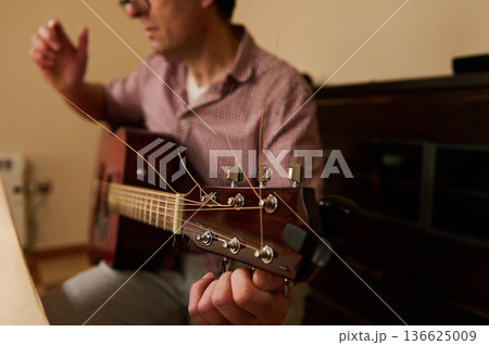 Man Changing Acoustic Guitar Strings at Home - Guitar Maintenance and Repair Practice 136625009