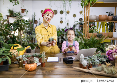 A woman and a young girl smile while holding potted plants in a plant shop A woman and a young girl smile while holding potted plants in a plant shop 136625298