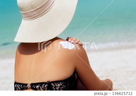 Woman applying sunscreen creme on tanned shoulder. Skincare. Sun protection sun cream. Bikini hat woman applying sunscreen lotion on back Woman applying sunscreen creme on tanned shoulder. Skincare. Sun protection sun cream. Bikini hat woman applying sunscreen lotion on back 136625712