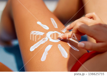 Sunbath protection. Woman using Suntan Lotion At The Beach In Form Of The Sun on leg 136625735