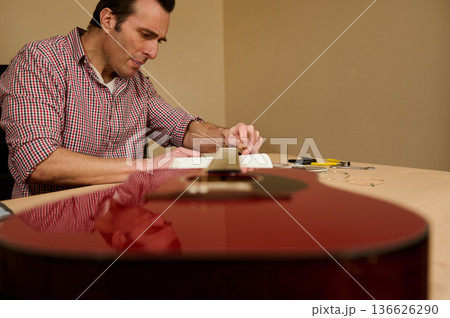 Man Changing Guitar Strings at a Table Focused on Maintenance and Repair Man Changing Guitar Strings at a Table Focused on Maintenance and Repair 136626290