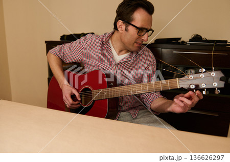 Man Adjusting Acoustic Guitar Strings at Home - Guitar Maintenance and Repair Practice 136626297