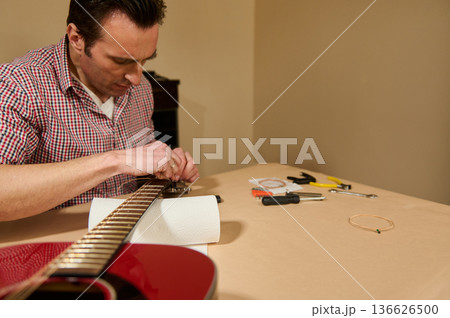 Man Restringing Acoustic Guitar With Tools - Guitar Maintenance and Repair 136626500