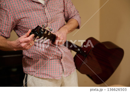 Man Adjusting Guitar Strings While Holding Acoustic Guitar - Guitar Maintenance and Repair 136626503