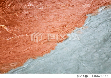 Two rivers meeting with distinct colors, one muddy brown and the other clear blue. Confluence of waters illustrating natural contrast. 136626837