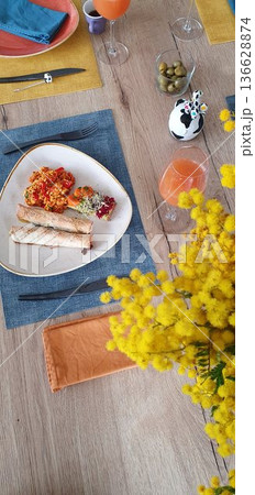Phone photo of a wooden table set for a colorful vegetarian lunch with dishes, orange juice, and mimosa flowers. Casual homemade meal scene with bright food, everyday dining, and relaxed lifestyle. 136628874