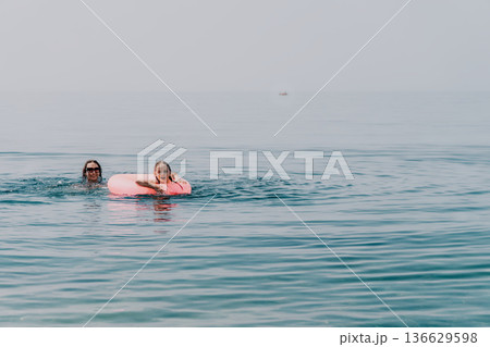 Mother daughter swimming mother and young daughter enjoying a sunny day at the sea with a pink inflatable ring 136629598