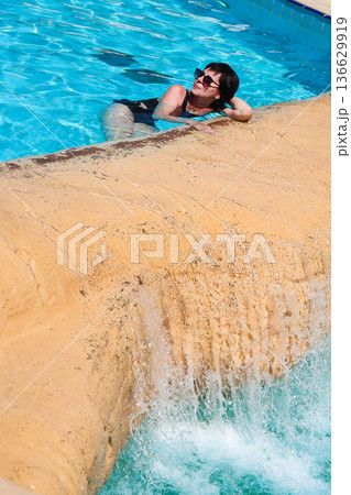 A woman swims in a pool with a waterfall A woman swims in a pool with a waterfall 136629919