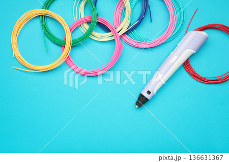 Children's 3D handle with plastic coils red, white, yellow, blue on blue background. Plastic PLA and ABS filament material for printing on a 3D pen Children's 3D handle with plastic coils red, white, yellow, blue on blue background. Plastic PLA and ABS filament material for printing on a 3D pen 136631367