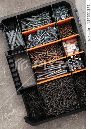Yellow case with small construction objects on grey background. Many storage compartments filled with builders accessories containing screws, nuts, bolts, nails and other tools in workshop. 136631381