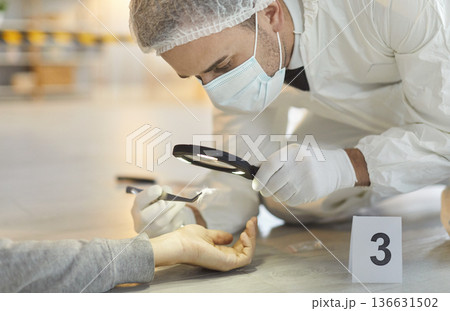 Forensic expert examining corpse hand with magnifying glass collecting evidence at the crime scene. Forensic expert examining corpse hand with magnifying glass collecting evidence at the crime scene. 136631502