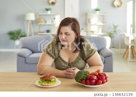 Dieting stout woman looking with temptation at delicious hamburger, trying to keep healthy nutrition Dieting stout woman looking with temptation at delicious hamburger, trying to keep healthy nutrition 136632139