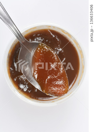 Spoonful of apricot jam over container vertical 136633406